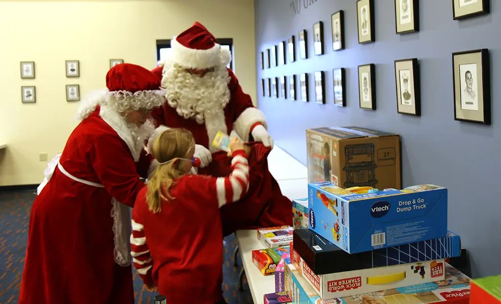 Girl putting an unwrapped toy into Santa's bag for the VSC toys and gift card drive.