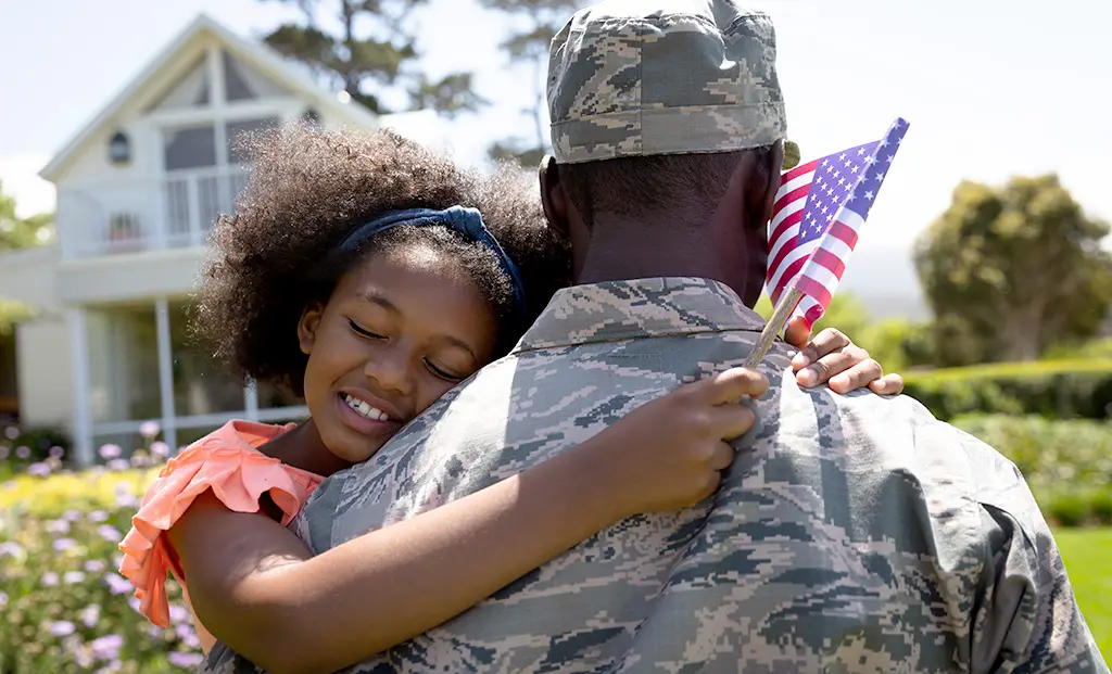 A young girl hugging a solider with american flag in her hand